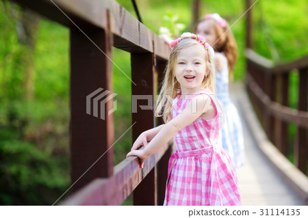 Two adorable sisters having fun on hanging bridge Two adorable sisters having fun on hanging bridge 31114135
