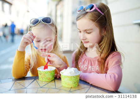 Two little sisters eat ice cream in outdoor cafe 31114138