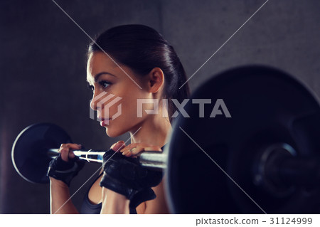 young woman flexing muscles with barbell in gym 31124999
