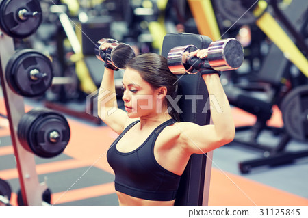 young woman flexing muscles with dumbbell in gym 31125845