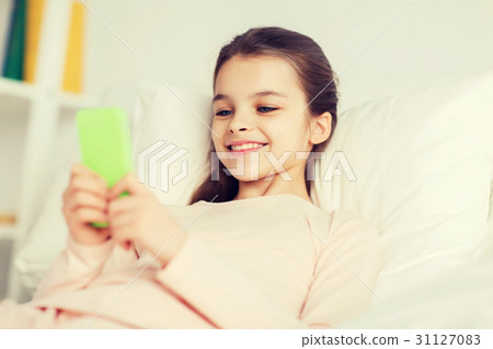 happy girl lying in bed with smartphone at home happy girl lying in bed with smartphone at home 31127083