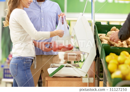 happy couple weighing tomatoes on scale at grocery happy couple weighing tomatoes on scale at grocery 31127250