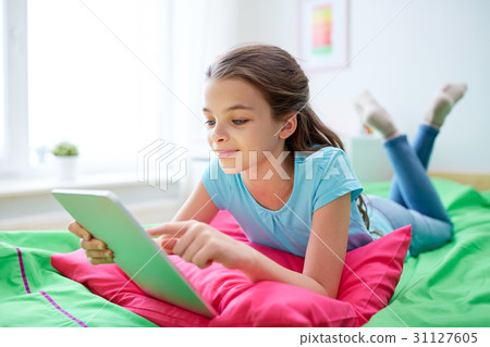 smiling girl with tablet pc lying in bed at home 31127605