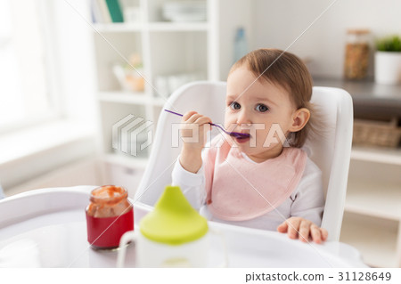 baby girl with spoon eating puree from jar at home 31128649