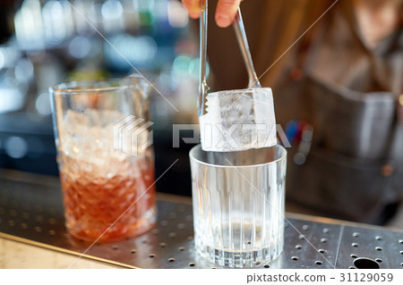 bartender adding ice cube into glass at bar 31129059