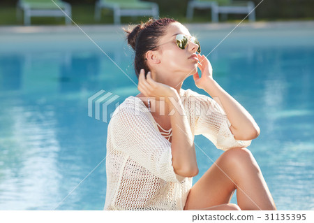 Beautiful young woman sitting by swimming-pool Beautiful young woman sitting by swimming-pool 31135395
