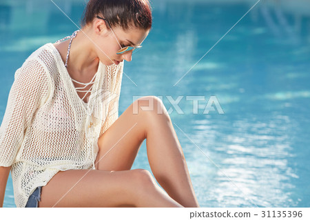 Beautiful young woman sitting by swimming-pool 31135396