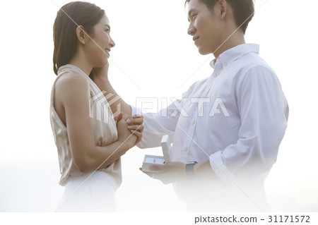 A man is holding a ring box and touching a woman's face. 31171572