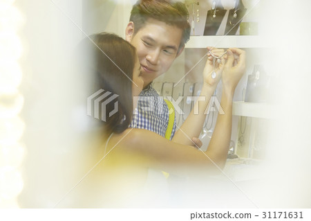 a man is looking a woman holding and looking a necklace in a shop a man is looking a woman holding and looking a necklace in a shop 31171631