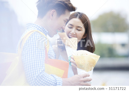 A couple is smiling and eatting two crepes outdoors. 31171722