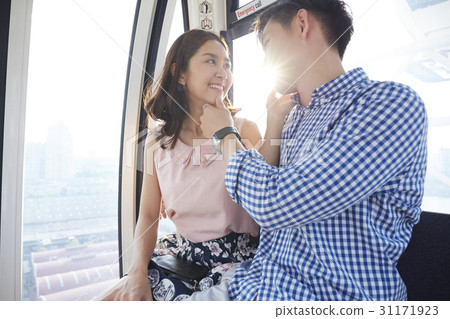 An Asian couple is touching each other's chin on a cable car. 31171923