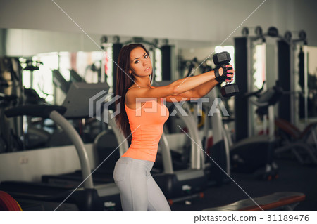 Brunette athlete lifts a dumbbell Brunette athlete lifts a dumbbell 31189476