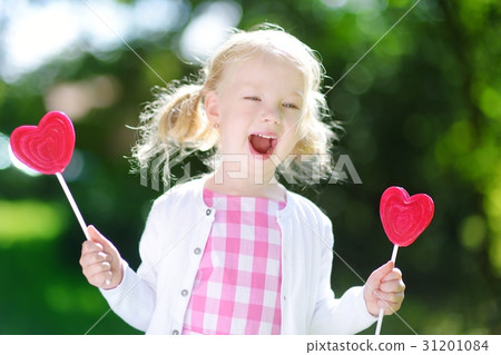 Cute girl eating huge heart-shaped lollipops 31201084