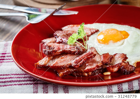 Slices of smoked bacon and fried egg on red plate Slices of smoked bacon and fried egg on red plate 31248779