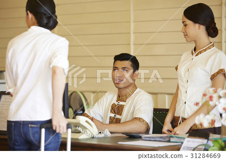 two receptionists are looking at the guest pulling her suitcase. two receptionists are looking at the guest pulling her suitcase. 31284669