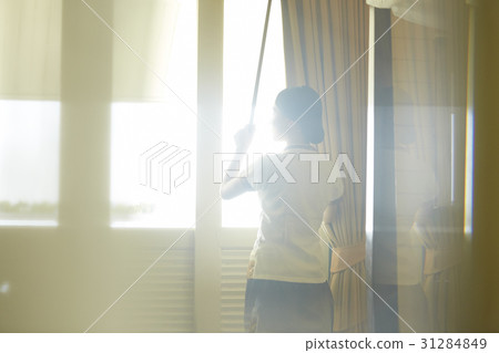 waitress is pulling up curtains in a hotel room. 31284849