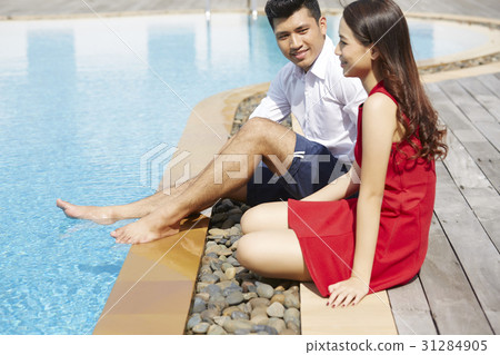 A couple is sitting, enjoying and smiling on a poolside A couple is sitting, enjoying and smiling on a poolside 31284905