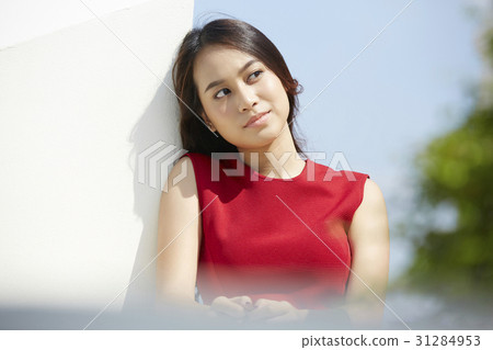 A woman in a red dress is leaning against the wall and looking. 31284953