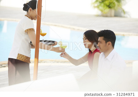 A couple is receiving cocktails from a waitress near a pool. A couple is receiving cocktails from a waitress near a pool. 31284971
