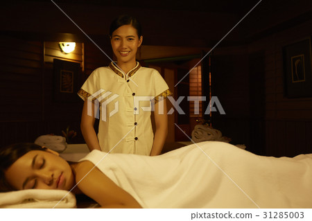 A happy therapist is standing beside a customer lying on bed in spas. 31285003