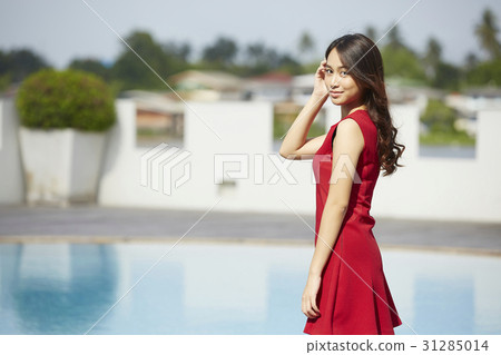 Beautiful woman in red dress is standing at poolside. 31285014