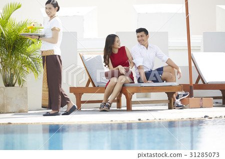 The couple is joking beside the pool and a waitress 31285073