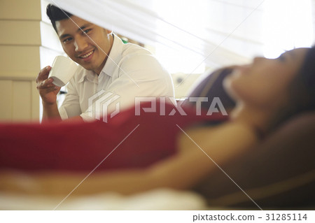 the man is drinking coffee and looking at a girl sleeping. the man is drinking coffee and looking at a girl sleeping. 31285114