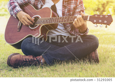 Man 's hand playing guitar, sitting on green grass 31291005