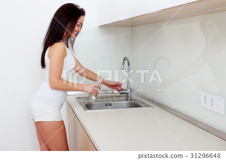 Woman Pouring Glass Of Water From Tap In Kitchen Woman Pouring Glass Of Water From Tap In Kitchen 31296648