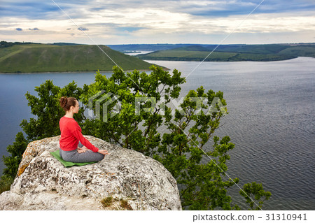 Young woman meditating in a lotus pose on the rock Young woman meditating in a lotus pose on the rock 31310941