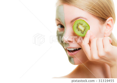 Woman in clay mask on face covering eye with kiwi Woman in clay mask on face covering eye with kiwi 31319455