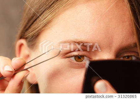 Woman tweezing eyebrows depilating with tweezers Woman tweezing eyebrows depilating with tweezers 31320865