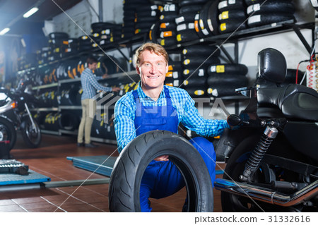 Mature mechanic holding new tyre for motorcycle Mature mechanic holding new tyre for motorcycle 31332616