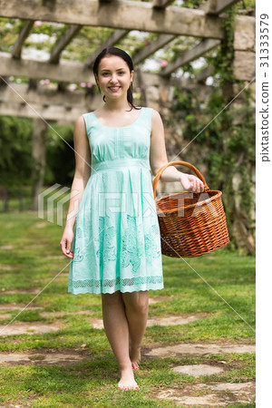 portrait of young woman holding a basket near roses in a garden 31333579