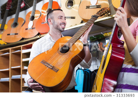 Friendly shopgirl helping male client to select guitar Friendly shopgirl helping male client to select guitar 31333693