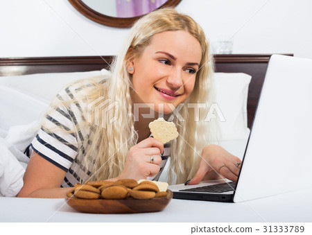 Cheerful young woman working on laptop in bed Cheerful young woman working on laptop in bed 31333789
