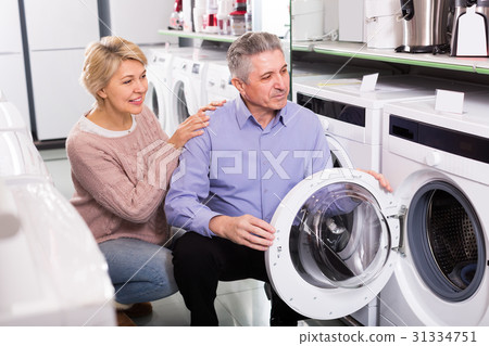interested mature couple chooses washing machine for their house in shop of household appliances interested mature couple chooses washing machine for their house in shop of household appliances 31334751