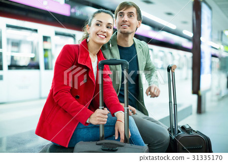 Young positive cheerful passengers with luggage waiting for train Young positive cheerful passengers with luggage waiting for train 31335170