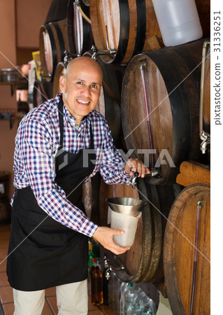 Seller pouring wine from wood barrel. 31336251