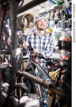 joyous man in helmet chooses for himself sports bike in bicycle shop joyous man in helmet chooses for himself sports bike in bicycle shop 31336992