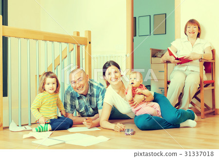 Smiling couple with their offspring and grandmother on floor at home in living room 31337018