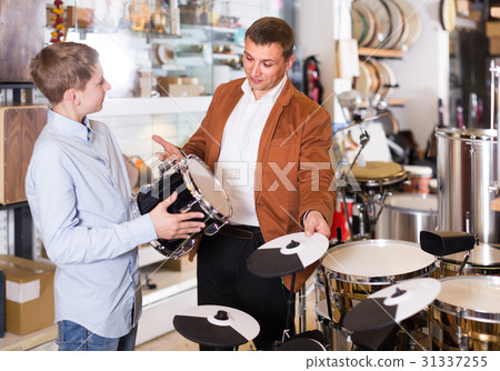 Father and teenage son examining drum units in guitar shop Father and teenage son examining drum units in guitar shop 31337255