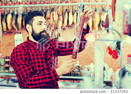 Young male customer examining sausages in butcher’s shop 31337263