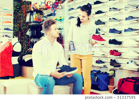female seller demonstrating sneakers to customer in sports store 31337595