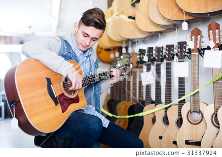 Male is choosing quality acoustic guitar 31337924