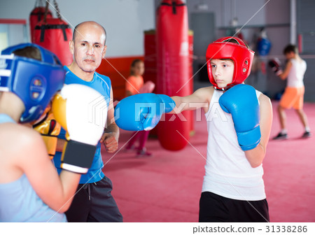 Boxing instructor closely follows the teenagers in sparring Boxing instructor closely follows the teenagers in sparring 31338286