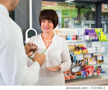 Smiling man pharmacist wearing uniform assisting customers Smiling man pharmacist wearing uniform assisting customers 31338611