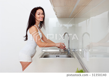 Woman Pouring Glass Of Water From Tap In Kitchen Woman Pouring Glass Of Water From Tap In Kitchen 31350140
