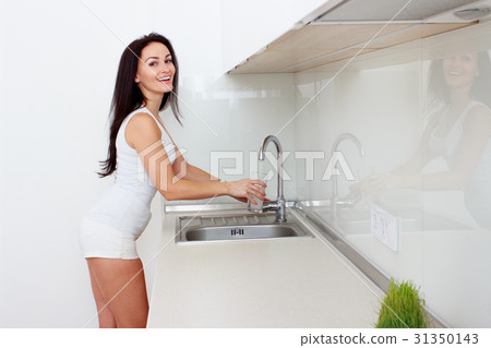 Woman Pouring Glass Of Water From Tap In Kitchen Woman Pouring Glass Of Water From Tap In Kitchen 31350143