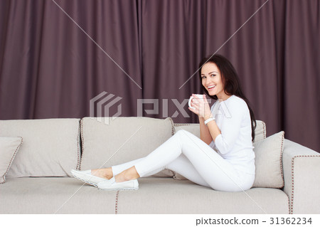 Portrait of beautiful young woman sitting on sofa Portrait of beautiful young woman sitting on sofa 31362234